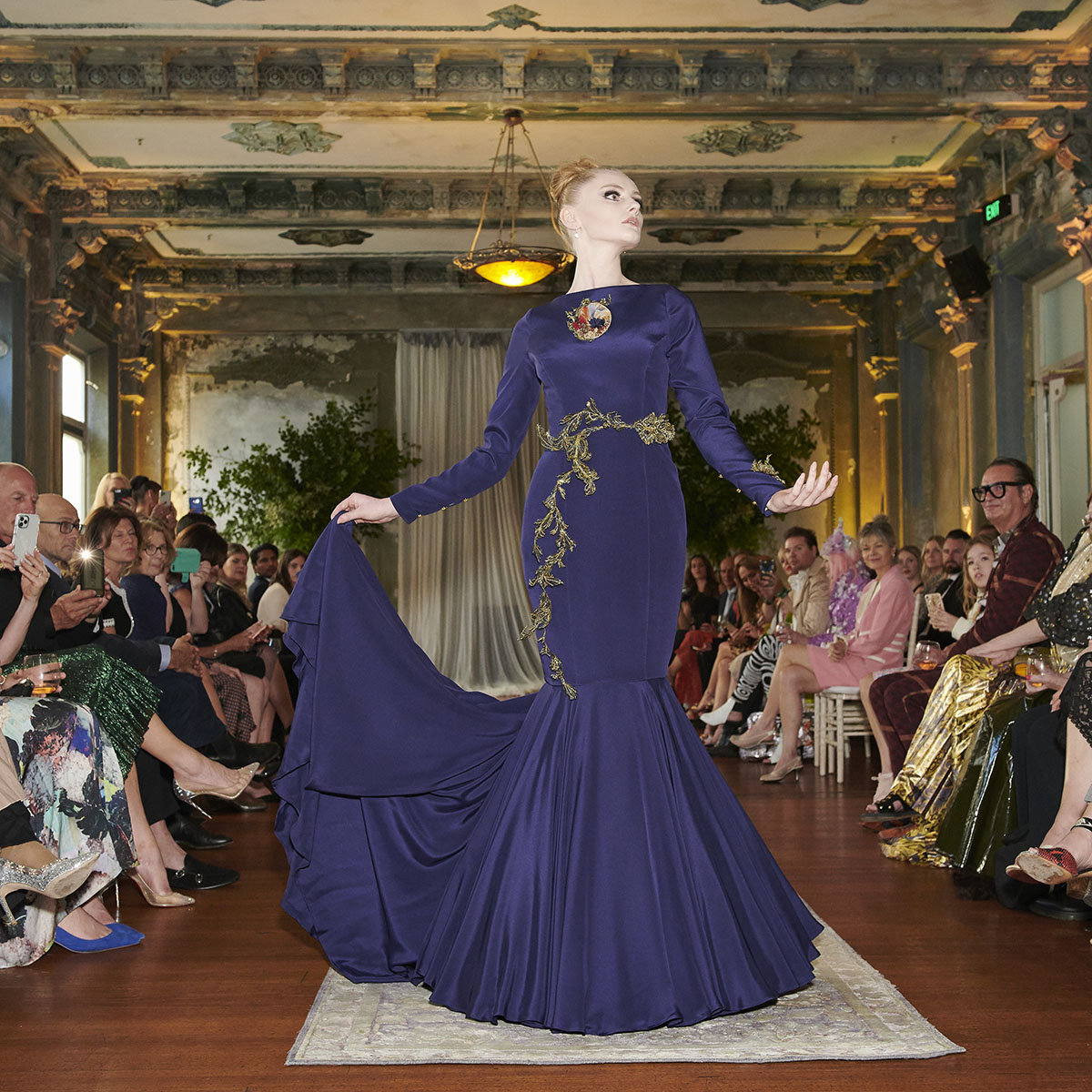 A navy blue crepe de chine dress featuring a sweeping fishtail train. The embroidery, a combination of golden French lace and wire, delicately wraps around the waistline of the dress. - DELPHINE GENIN